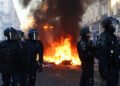 A fire burns, as Police officers in riot gear stand guard, during civil unrest, the day after a national day of demonstrations against the cost of living and rising fuel prices, in Paris, France.