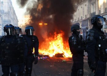 A fire burns, as Police officers in riot gear stand guard, during civil unrest, the day after a national day of demonstrations against the cost of living and rising fuel prices, in Paris, France.